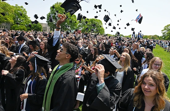 Graduates celebrating outdoors and tossing caps in the air at commencement.
