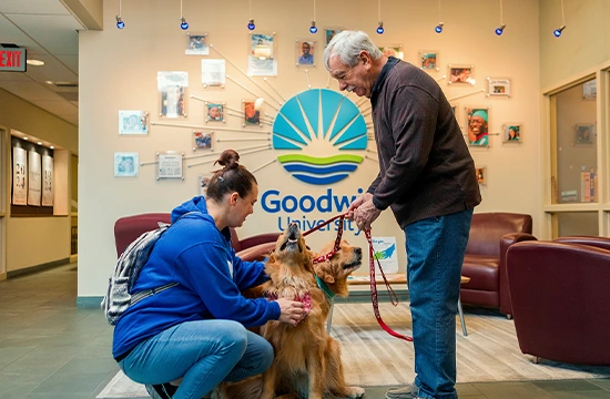Student and older man interacting with two dogs in a Goodwin University lobby
