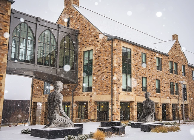 Campus building and sculptures in a courtyard during snowfall