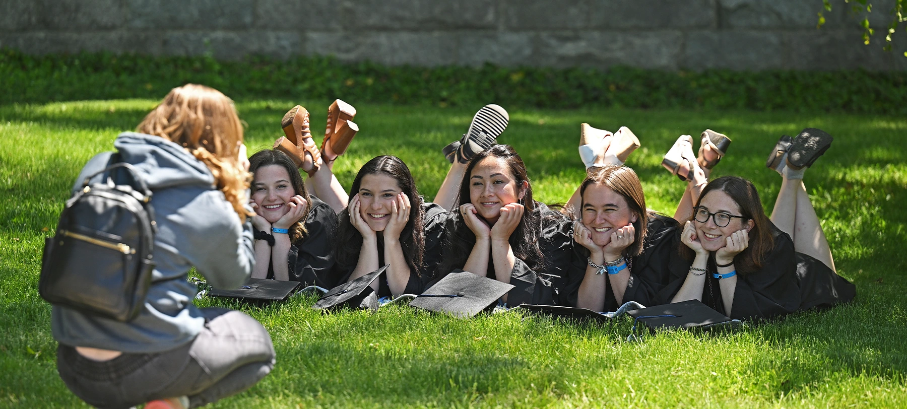 Graduates in caps and gowns lying on grass while posing for a photo outdoors