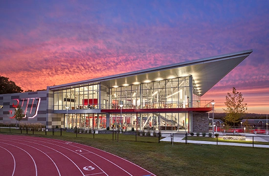 Modern university building with glass facade beside a running track at sunset.